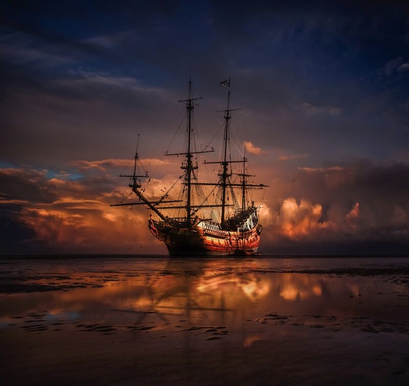 Navio pirata navegando em águas caribenhas ao pôr do sol, evocando a Era de Ouro da Pirataria