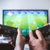 Controle de videogame prateado caindo no chão com movimento borrado, fundo neutro.