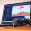 Desenvolvedores em estúdio de games trabalhando em estações com telas de computador exibindo cenas de ação.