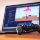 Desenvolvedores em estúdio de games trabalhando em estações com telas de computador exibindo cenas de ação.
