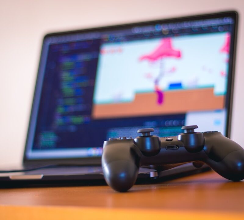 Desenvolvedores em estúdio de games trabalhando em estações com telas de computador exibindo cenas de ação.